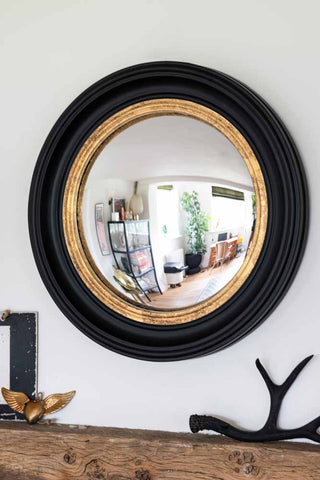 lifestyle image of black and gold framed convex mirror hanging above a mantel piece