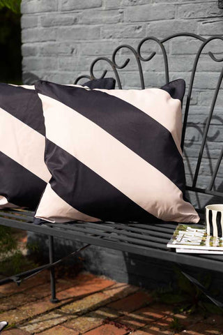 Lifestyle image of the Black & Natural Stripe Outdoor Cushion on a garden bench.
