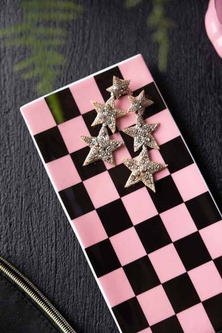 Close-up image of Black & Pink Checkerboard Trinket Dish with star earrings on, styled on a black table. 