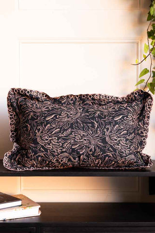 The Black & Pink Tiger Cushion With Pretty Scalloped Edge on a black surface, styled with some books and a plant.