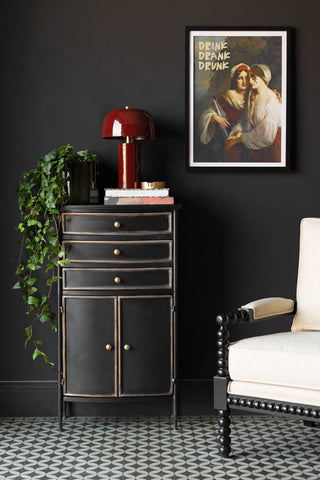 A styled image of the Black & Gold Antiqued-Style Side Cabinet against a black wall with a plant on it.