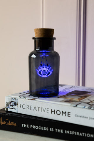 The Blue Eye Neon Bottle Light displayed on a stack of books.