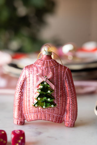 Pink sweater-shaped Christmas ornament with a tree design on a marble surface.
