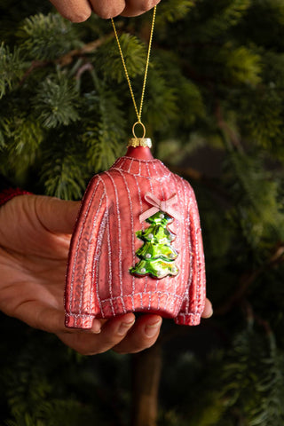 Pink textured sweater ornament with a green tree design held against a green background