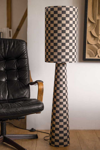 Lifestyle image of the Charcoal & Natural Checkerboard Floor Lamp against a light background next to a black leather armchair