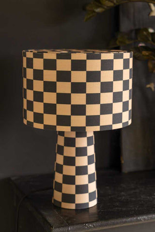 Lifestyle image of the Charcoal & Natural Checkerboard Table Lamp against a dark background