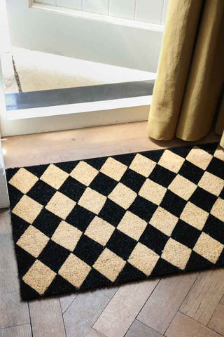 The Checkered Patterned Doormat on the floor in front of an open door and door curtain.