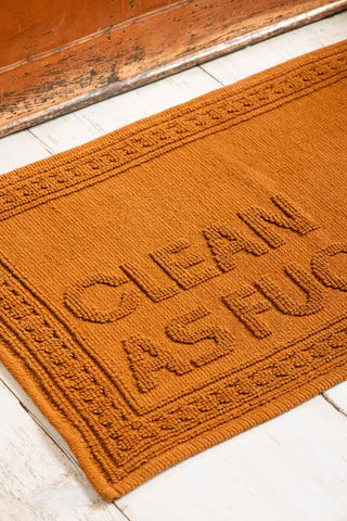 Brown bath mat with 'clean as fuck' on it.