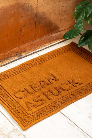 Brown bath mat with text on a wooden floor.