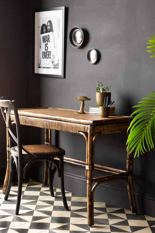 The Dark Brown Rattan Console styled with various home accessories, on a geometric floor next to a black wall, with a chair.