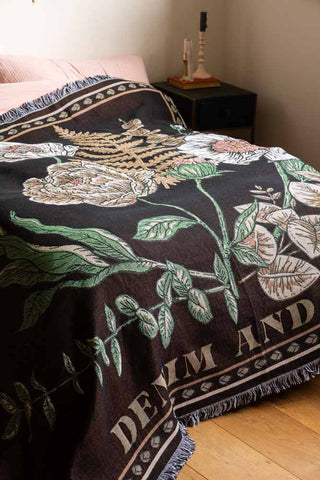 Close-up of the Denim & Bone Scandi Black Woven Cotton Throw styled on a bed, with some candlesticks and a book on a bedside table in the background.