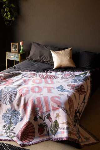 The Denim & Bone You Got This Woven Cotton Throw styled on a bed in a black bedroom.