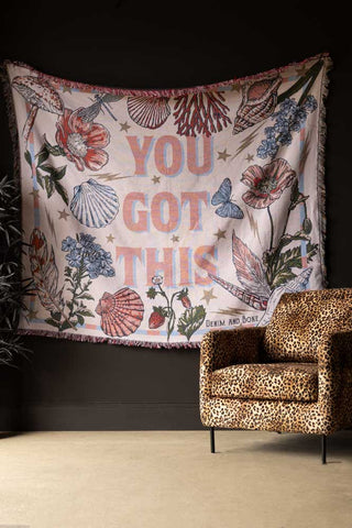 The Denim & Bone You Got This Woven Cotton Throw displayed hanging on a black wall, styled with a leopard print chair and a plant.