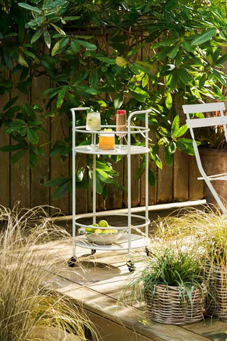 The Effortless Outdoor Drinks Trolley in Clay styled with various drinks and a bowl of fruit on, on outdoor decking with plants.