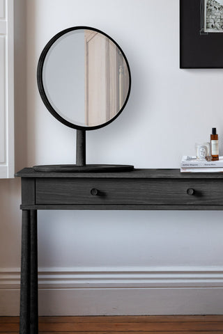 Close-up of the Elegant Black Dressing Table with some magazines and accessories on, with a print on the wall in the background.