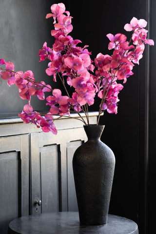 The faux fuchsia flower stems in a black vase.