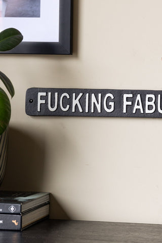 Close-up of the Fucking Fabulous Sign displayed on a neutral wall with a framed artwork, next to a potted plant and some books.