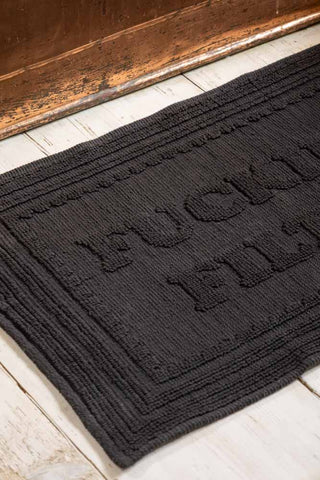 Close-up of a black bath mat with text on, displayed on a wooden floor.