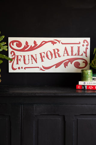 Decorative sign with 'Fun for All' text on a black surface with greenery