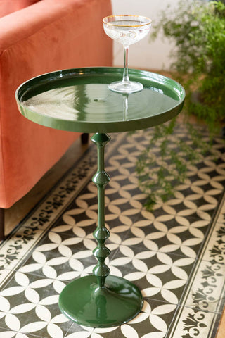 Green side table with a glass on a patterned floor