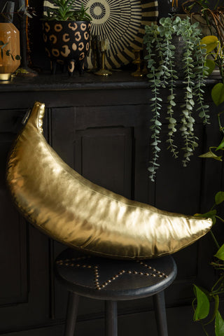 The Gold Banana Cushion displayed on a black star stool in front of a black sideboard styled with various home accessories and plants.
