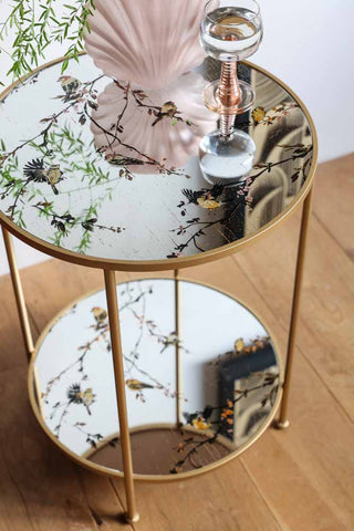 Lifestyle image of the Gold Beautiful Birds Mirror Side Table styled with decorative accessories.