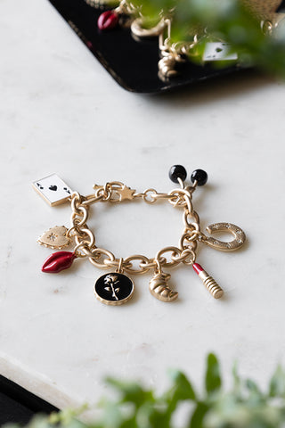 The Gold Chunky Chain Charm Bracelet on a table,with some other jewellery in a trinket tray and some plants.