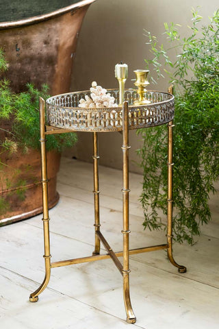 The Gold Distressed Mirrored Side Table displayed in a bathroom with an ornament and candlestick holders on the top, with a plant to the side of the shot.