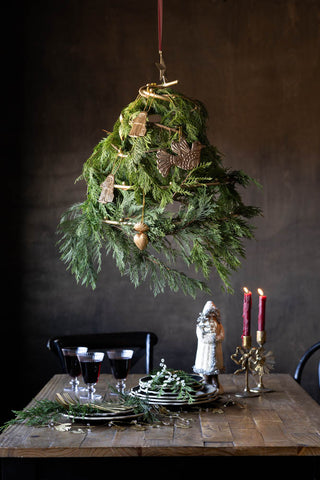 The Gold Hanging Christmas Frame for Decorations styled with various greenery and gold decorations on, styled above a Christmas tablescape with tableware and lit candles.