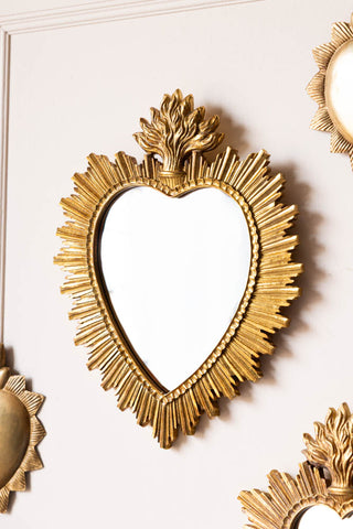 The Gold Sacred Heart Ornate Mirror on a plain wall with other small mirrors.