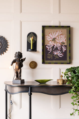The Gold Milagro Heart Candlestick Wall Sconce on the wall, styled with various other decorative accessories and some greenery.