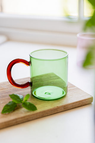The Green & Red Glass Mug on a wooden board with some mmint leaves.