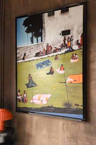 Lifestyle image of the HKliving Endless Summer Framed Artwork displayed on a dark wood wall and styled with a side table and table lamp. 