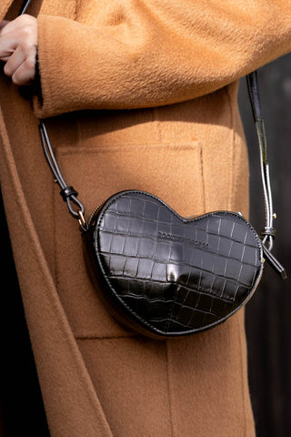 A black heart shaped bag being worn by a model.