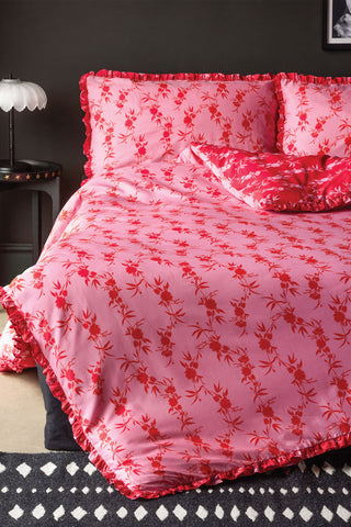 The Hot Pink Floral Frill Duvet Cover and Pillow Case Set styled on a bed in front of a black wall.
