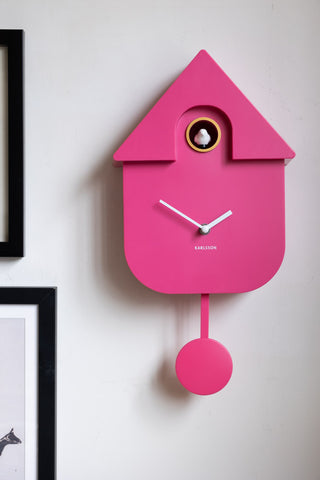The Hot Pink Modern Cuckoo Wall Clock displayed on the wall with some framed artworks.