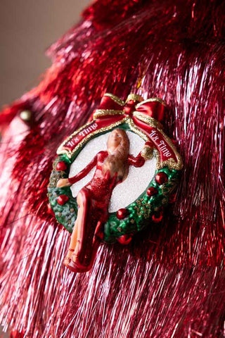 A christmas tree decoration hanging in front of some red tinsel.