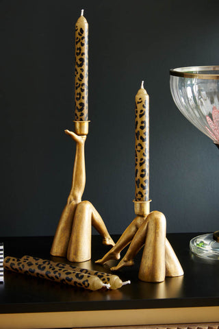 Lifestyle image of two different leg candle holders displayed on a sideboard with leopard print candles and a table lamp.