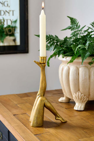 Lifestyle image of the Kick Leg Candle Holder with a lit candle inside, displayed on a wooden sideboard with a planter.