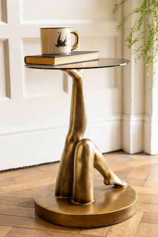 A styled image of the Gold Kicking Legs Side Table with Glass Top with a mug on top of it.