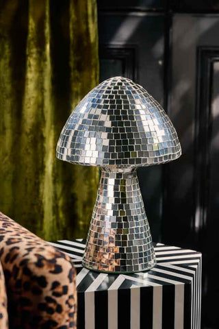The Large Disco Mushroom Ornament displayed on a striped side table next to a sofa and curtain.