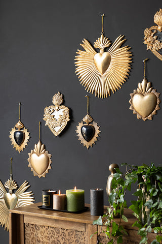 The Large Milagro Antiqued-Style Heart Decoration hanging on a black wall with various other heart decorations, styled above a sideboard with candles and greenery on.