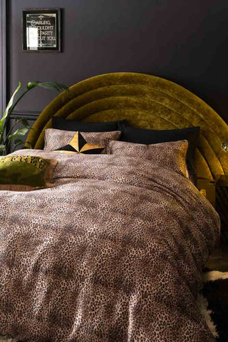 Lifestyle image of the Leopard Love Duvet Cover and Pillow Case Set styled on a bed with a velvet headboard, with cushions, a plant and decorative mirror in the shot.