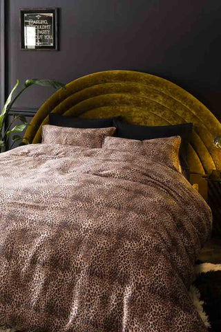 Lifestyle image of the Leopard Love Duvet Cover and Pillow Case Set styled on a bed with a velvet headboard, with a plant and decorative mirror also in the shot.