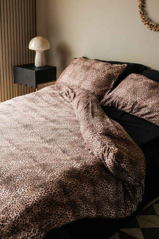 Lifestyle image of the Leopard Love Duvet Cover and Pillow Case Set styled with a mushroom table lamp in front of a cream wall.