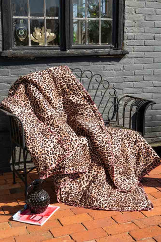 The Leopard Print Scalloped Edge Quilt on an outdoor bench on a patio, styled with a magazine and a jug.