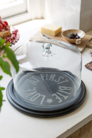 A styled image of the Marble Cheese Board & Glass Cover on a kitchen worktop with cheese in the background.
