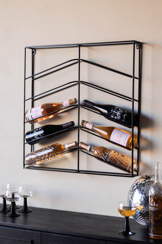 The Matte Black Metal Wine Rack styled with various wine bottles on, above a bar with wine glasses, a bottle and a disco ball.