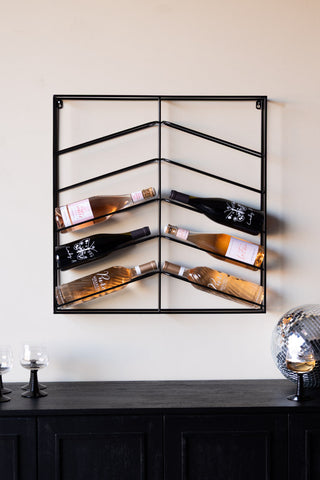 The Matte Black Metal Wine Rack on a neutral wall, styled with wine bottles, glasses and a disco ball.