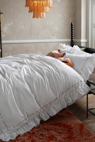 Lifestyle image of the White Mega Frill Duvet Cover and Pillowcase Set styled on a bed in a bedroom with various home accessories. 